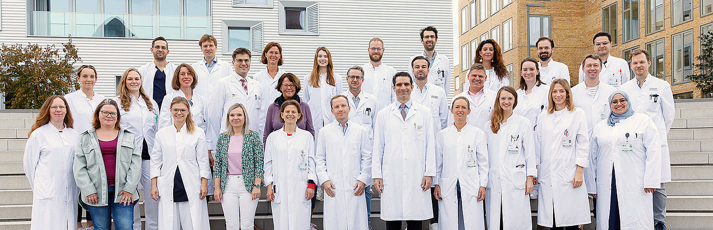 Chirurgie Gruppe von Ärzten und medizinischem Personal in weißen Kitteln posiert auf Treppe vor einem modernen Gebäude.