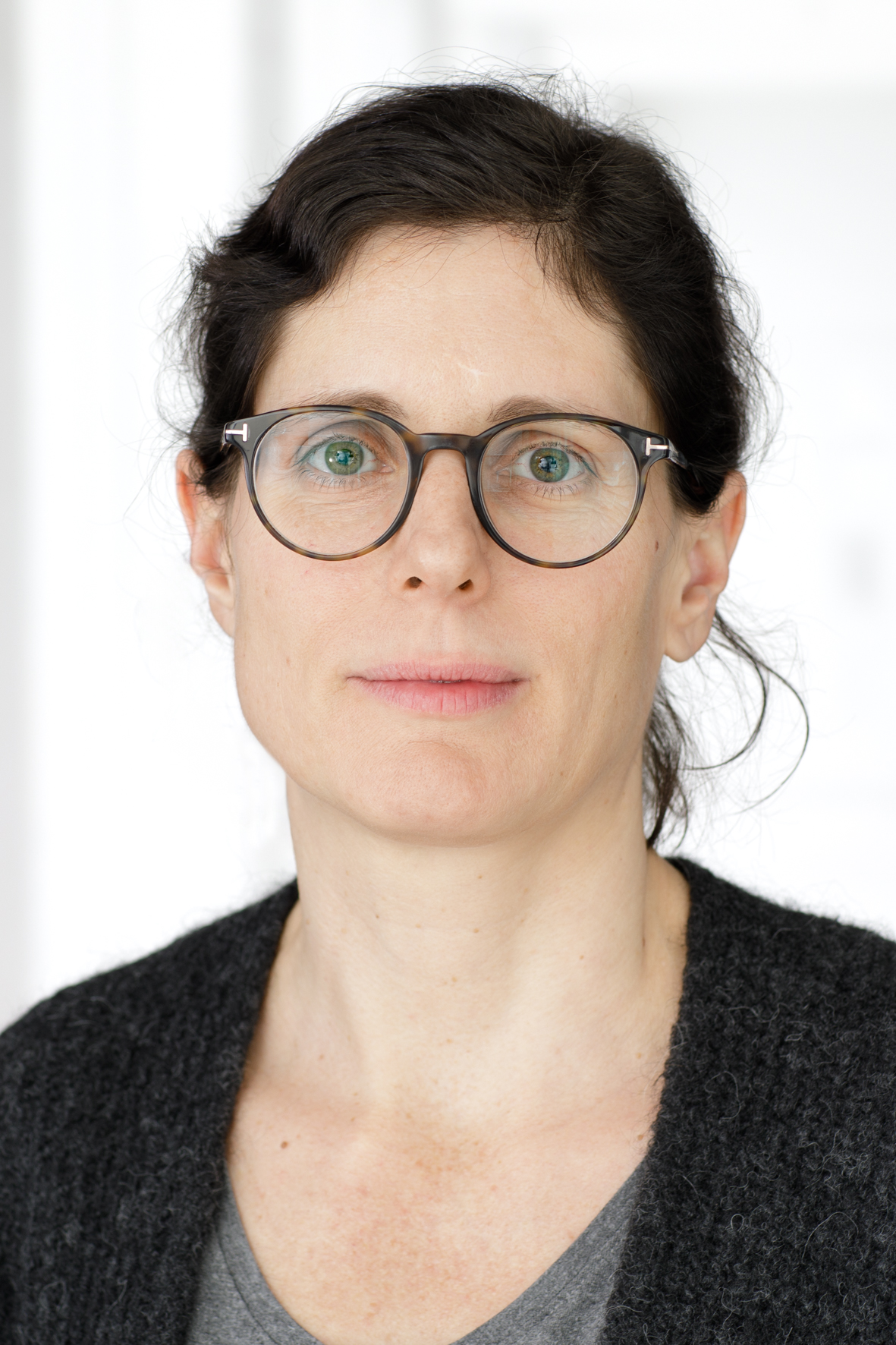 Frau mit Brille und dunklem Haar schaut direkt in die Kamera; sie trägt einen grauen Pullover.