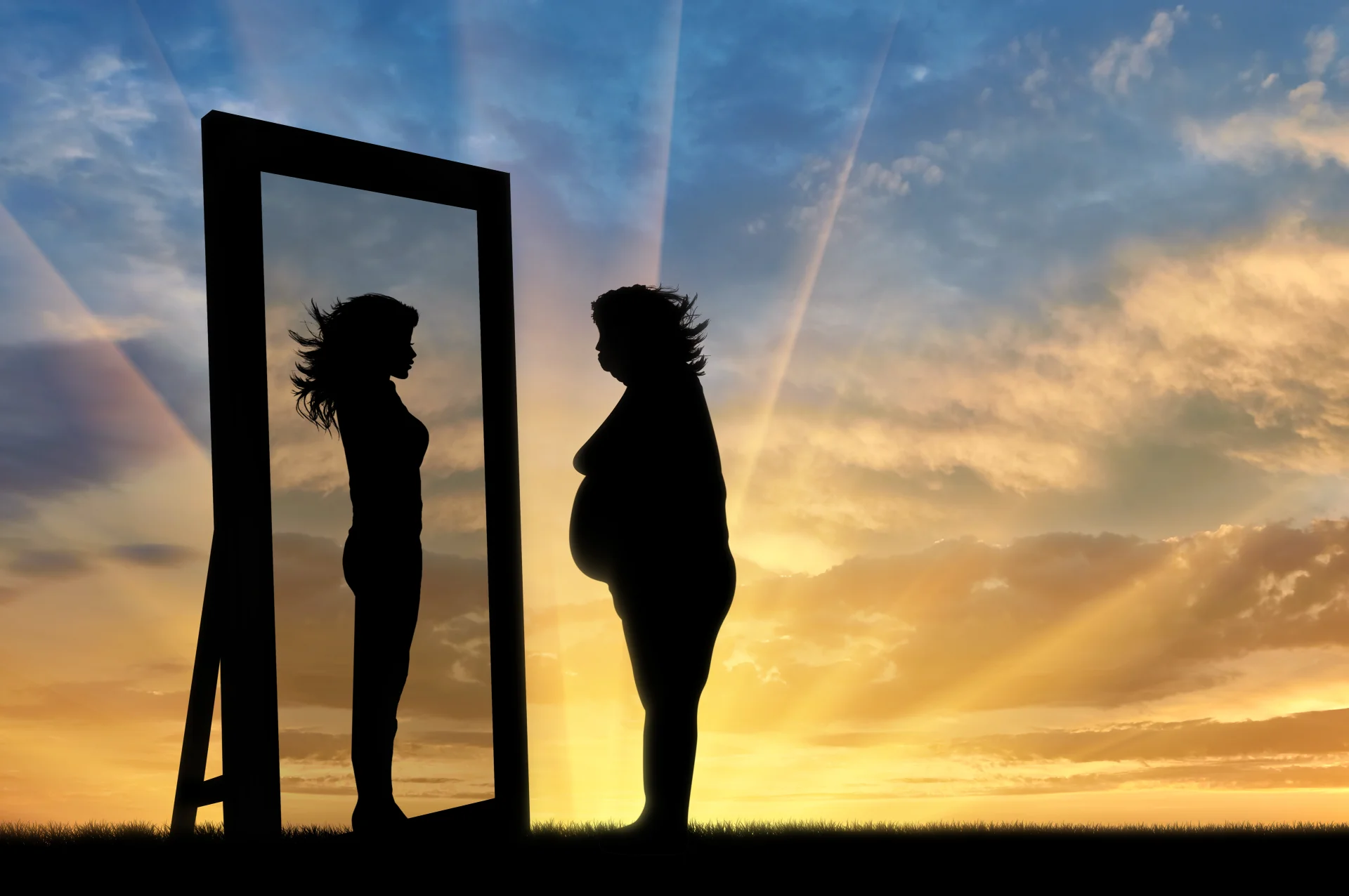 Silhouette einer Person vor einem Spiegel: sieht sich als schlank, im Hintergrund ein Sonnenuntergang.